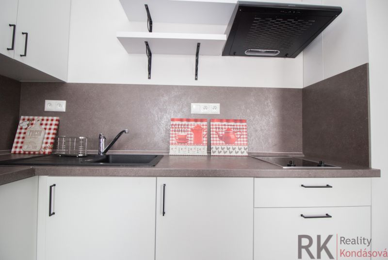 A kitchen in a studio apartment with a brown countertop and decorative tiles.