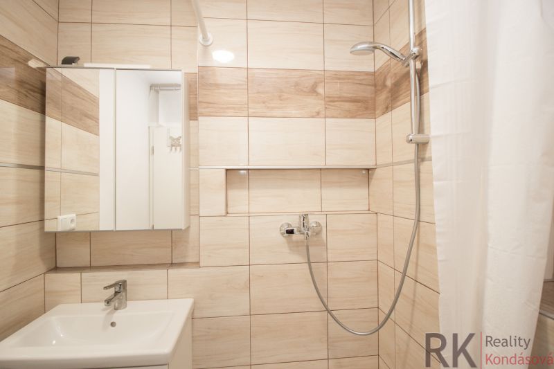 Bathroom in a studio apartment with a white sink and shower, light tiles.