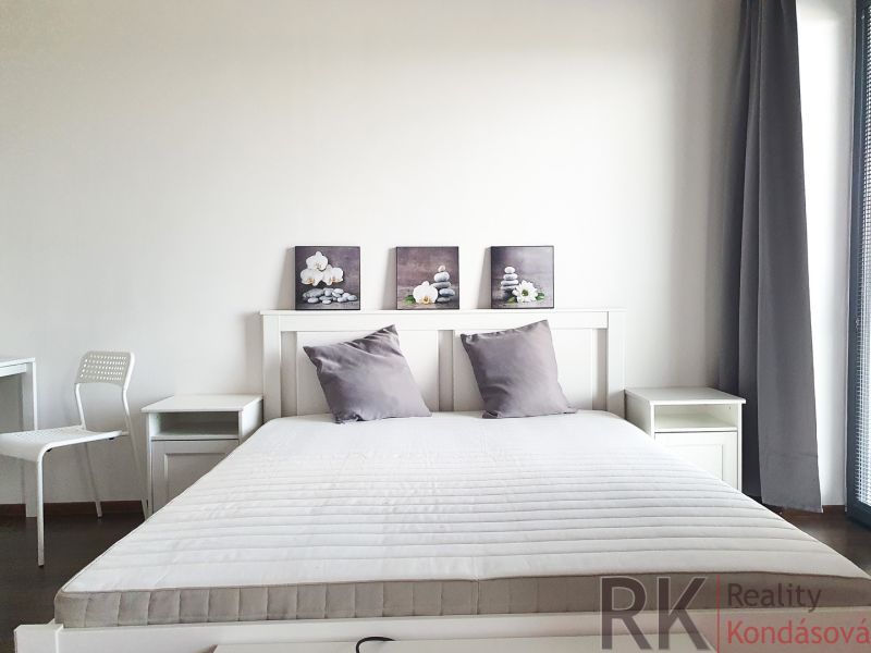 Bright bedroom with a white bed, wall decorations, and a wood-patterned floor.
