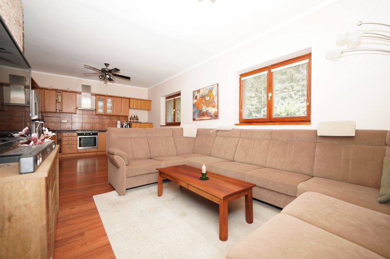 Living room in a family house with a sofa, wooden table, and kitchen in the background.