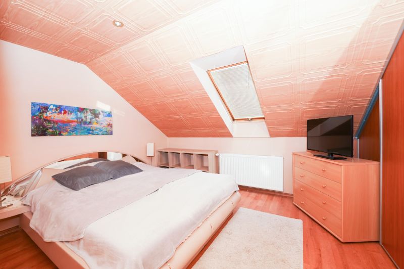 Attic bedroom with a bed, television, and wood-patterned flooring in a family house.