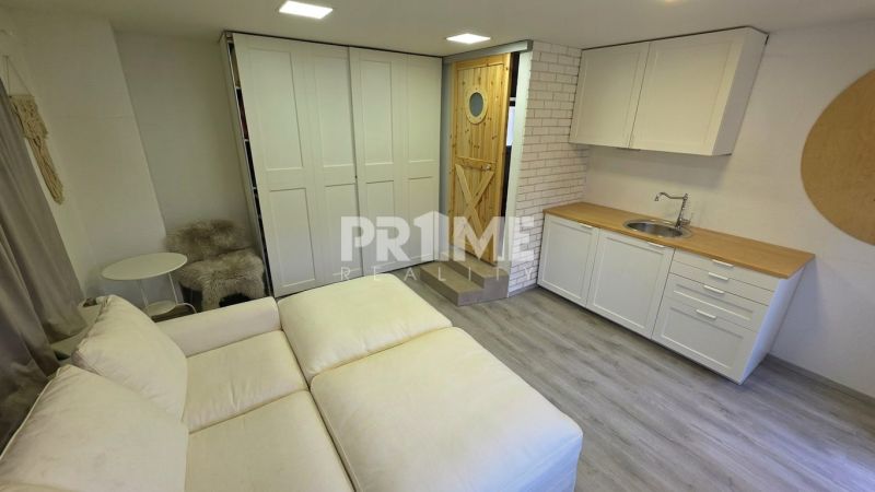 Living room in a family house with a sofa, kitchen unit, and floor with wooden decor.