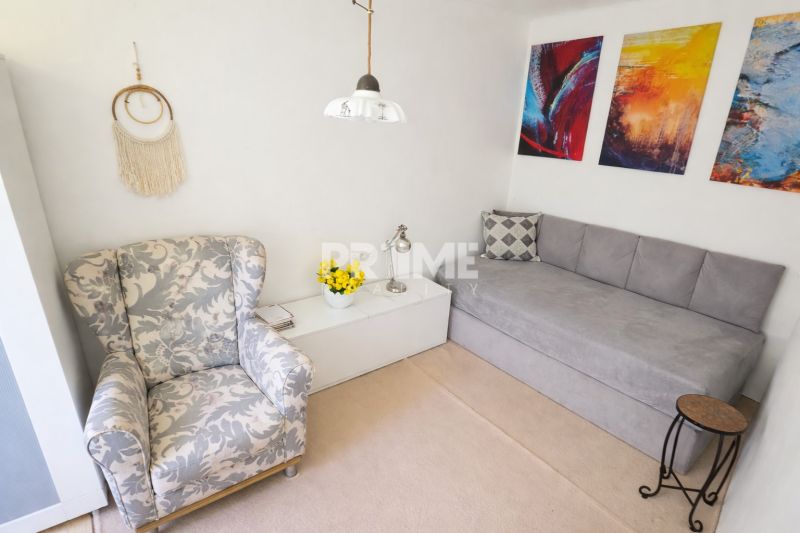 Living room in a family house with a floral armchair, gray sofa, and colorful paintings on the wall.