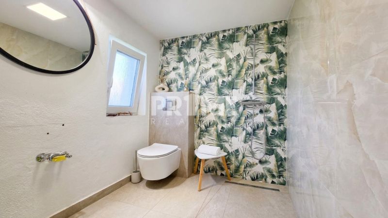 Bathroom in a family house with leaf-patterned tiles and a wall-mounted toilet.