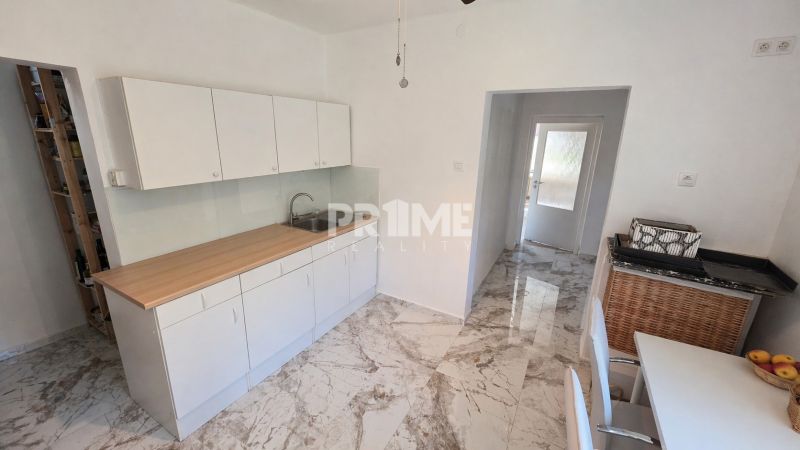 A bright kitchen in a family house with white cabinets and a marble floor.