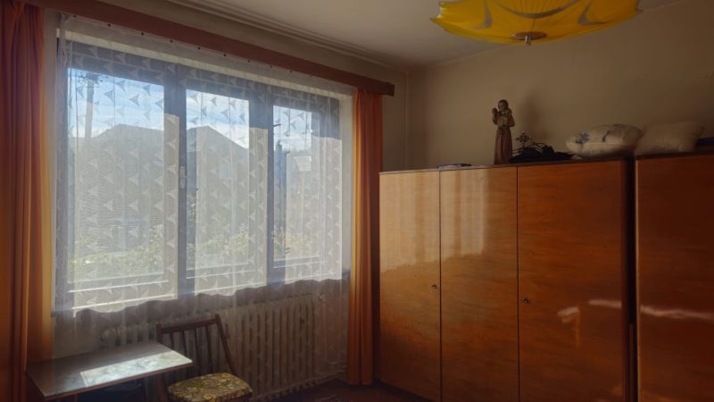 A room in a family house with a wooden wardrobe and a window with a lace curtain.