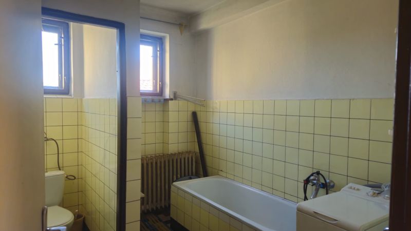 A bathroom in a family house with a bathtub, light tiles, and two windows.