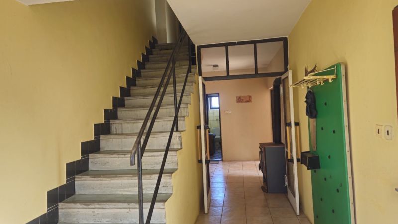 Interior of a family house with a tiled stove, staircase, and wall-mounted coat rack.