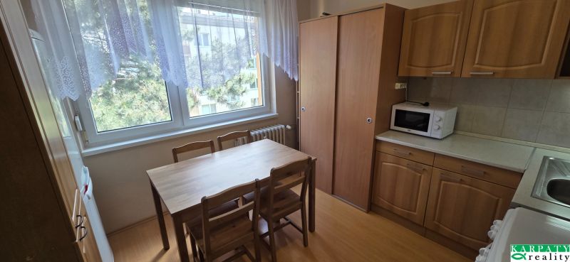 A kitchen in a one-room apartment with a wood-patterned floor, table, and cabinets.