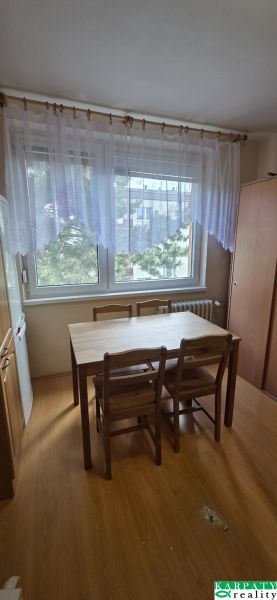 Dining area with a table and chairs, floor with wood decor, curtain on the window.