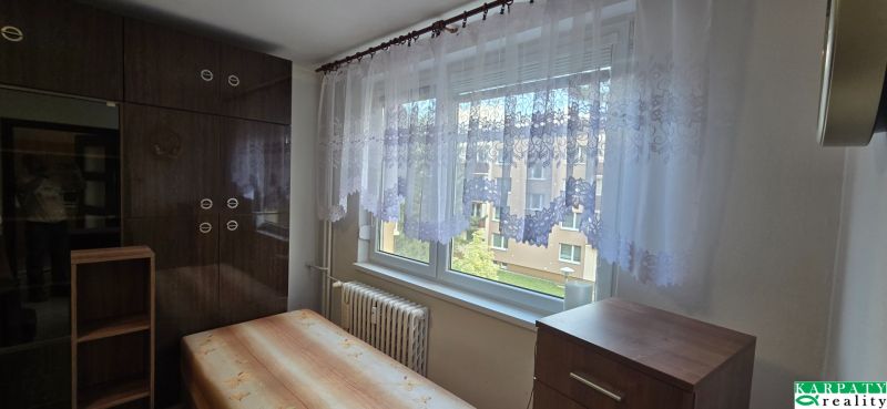A room in a one-bedroom apartment with a wooden wardrobe, a bed, and curtains on the window.