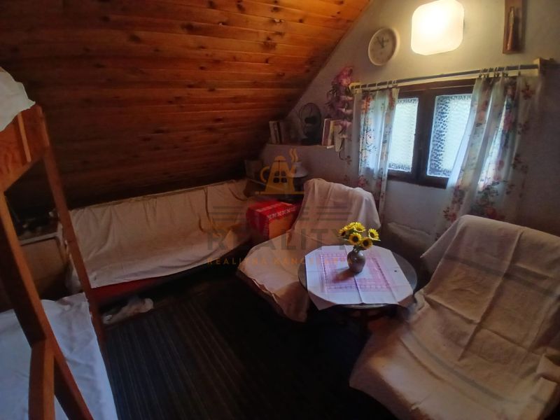 A room with a slanted ceiling, armchairs, a table with a tablecloth and flowers, wooden paneling.
