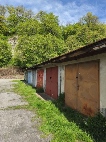 Row garages on Dlhá Street in Prievidza, with greenery and trees in the background.
