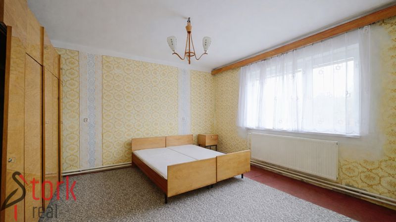 A bedroom with wallpaper, wooden furniture, and a large window in a family house.