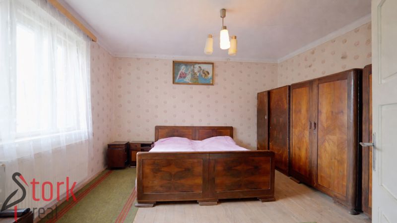 A bedroom in a family house with wooden furniture and a bed, wallpapered walls, and a floor with a wooden decor.