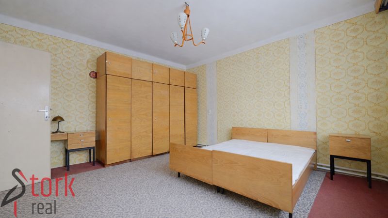 A bedroom in a family house with wallpaper, wooden furniture, and a gray carpet.