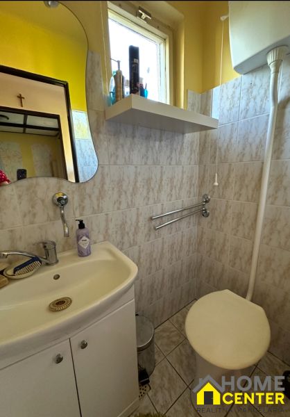 Bathroom with a mirror, sink, and toilet, tiled with light tiles.
