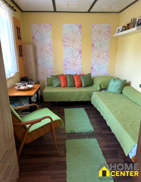 A sofa in a green cover and a wall with floral wallpaper on a floor with wooden decor.
