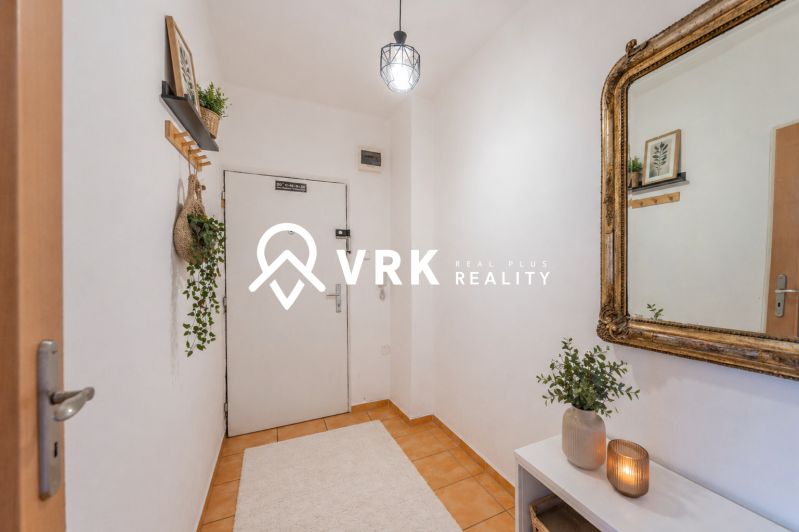 A hallway in a 2-room apartment with decorations, a mirror, and plants, with a carpet on the floor.
