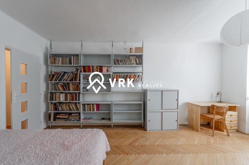 Living room in a 2-room apartment with a bookshelf, a desk, and a wooden decor floor.