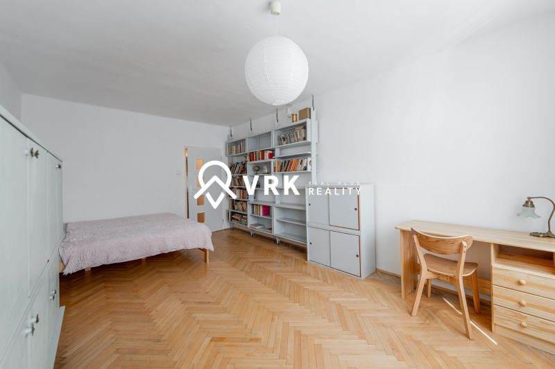 A room with a bed, bookshelf, table, and a floor with a wooden decor in a 2-room apartment.