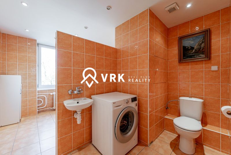 A bathroom in a 2-room apartment with a washing machine, toilet, and window, decorated in orange tones.