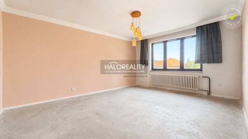 Spacious living room of a family house with a large window and radiator, beige walls, pendant lights.
