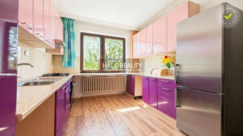 A kitchen with purple and pink cabinets, a wooden-patterned floor, a large window.