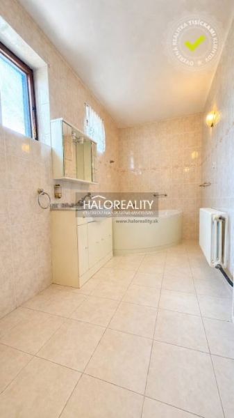 A bathroom in a family house with a bathtub, tiles, and white furniture.