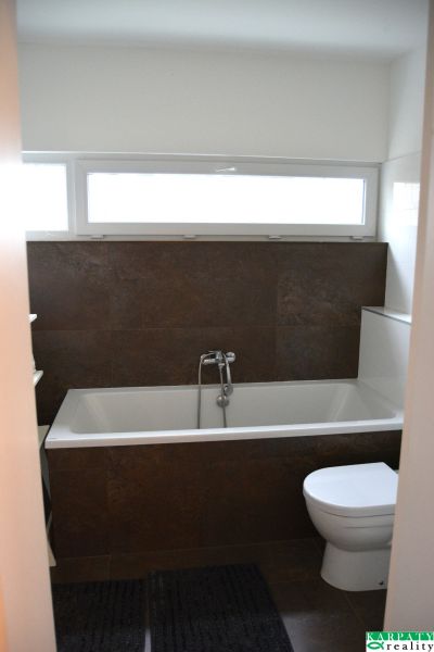 A bathroom in a family house with a bathtub, black tiles, and a bright window.