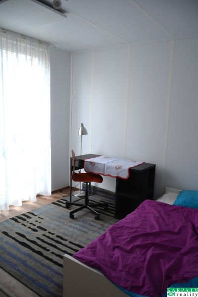 Bedroom in a family house with a desk, wooden decor flooring, and a bed.