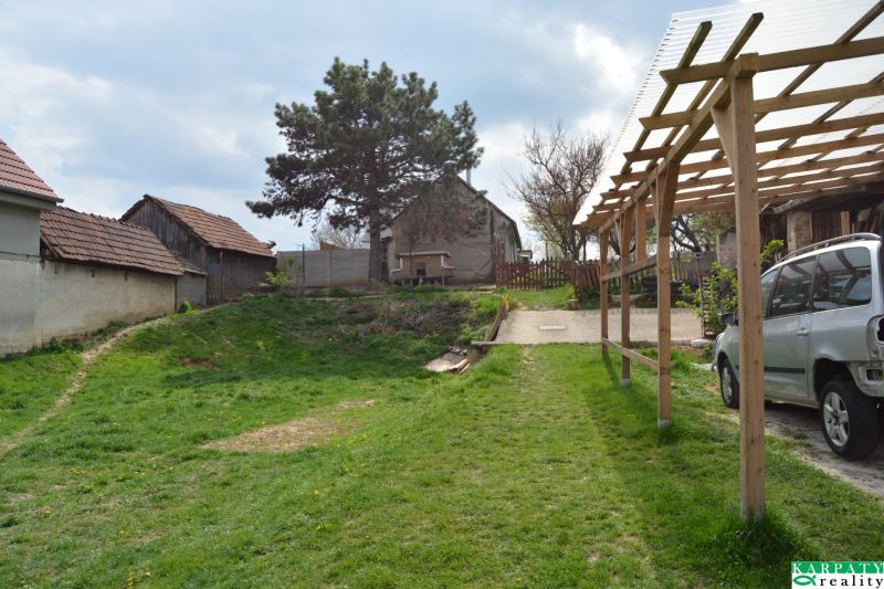 The courtyard of a family house in Nižná with a car, a shelter, and greenery.