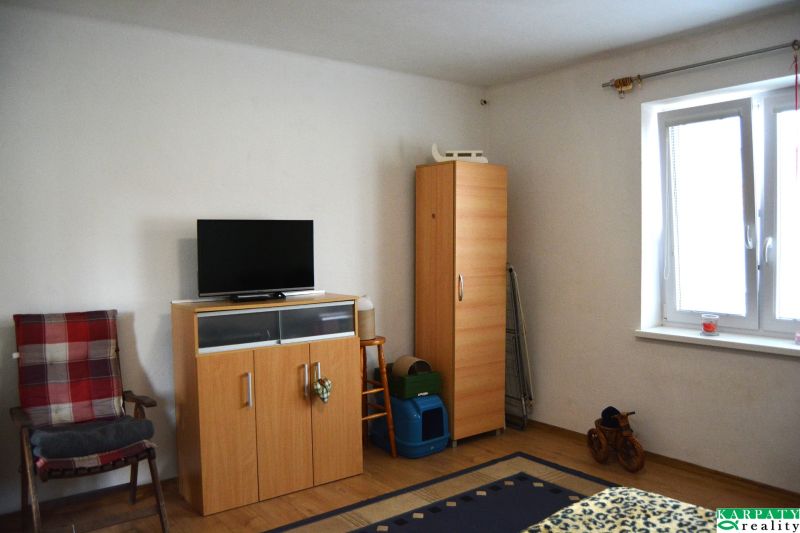 A room with furniture, a television, white walls, and a floor with a wooden decor.
