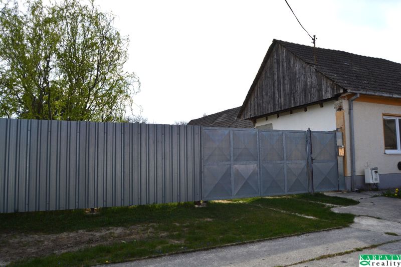 A family house in Nižná with a metal fence and gate, standing next to a tree.