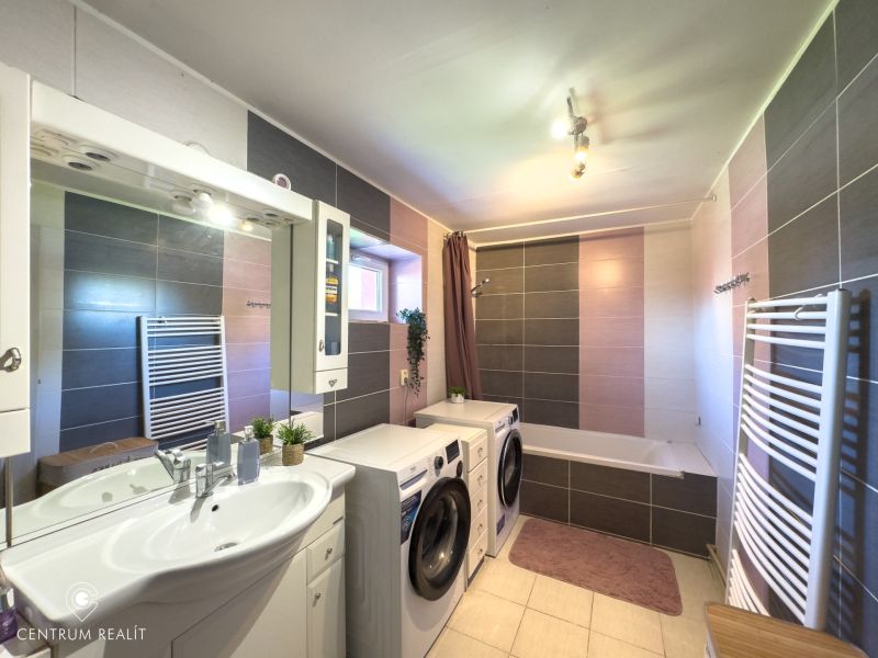 A bathroom in a family house with a washing machine, a bathtub, and tiled walls.