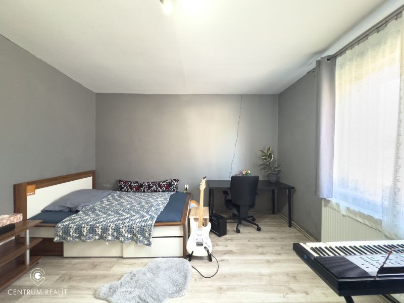 Bedroom in a family house with a bed, table, guitar, and keyboard, wooden decor flooring.