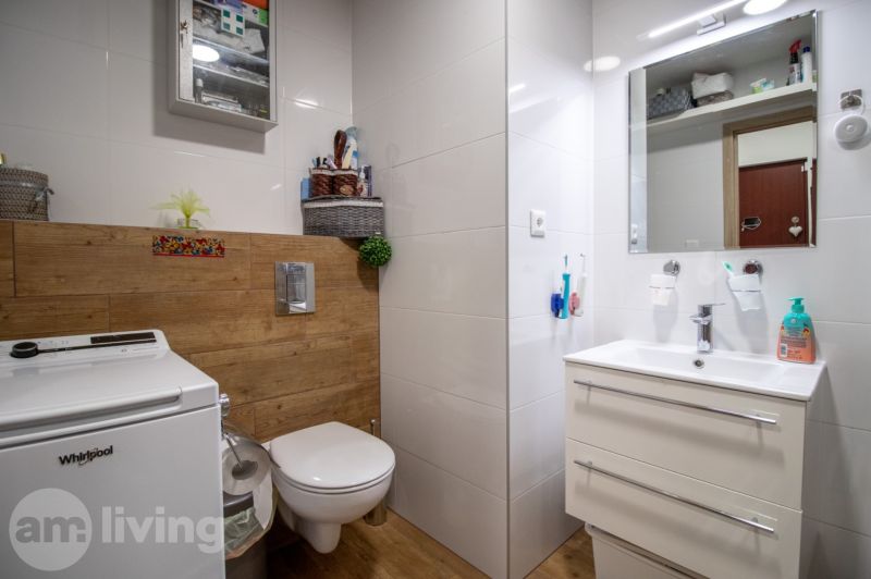 A bathroom in a 2-room apartment with a shower, washing machine, and a floor with a wooden decor.