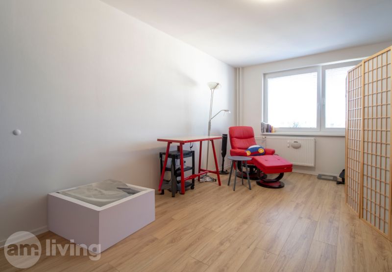 A room in a 2-room apartment with an armchair, a table, and a floor with a wooden decor.