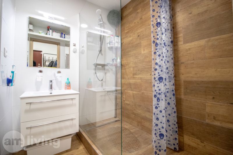 A bathroom in a 2-room apartment with a wooden decor floor, a shower corner, and a sink.