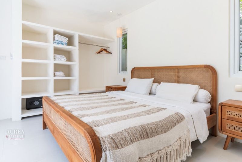 A bright bedroom interior in a villa with a wicker bed and white furniture.
