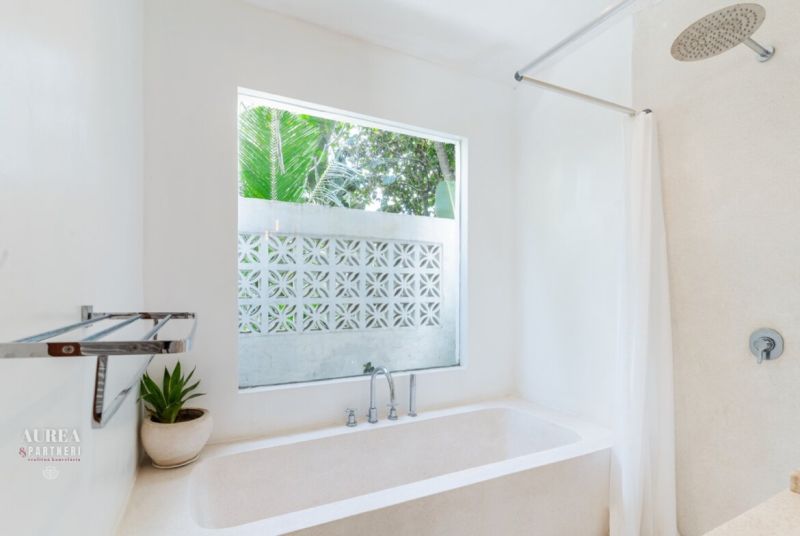 A villa bathroom with a bathtub, large window, and a potted plant.