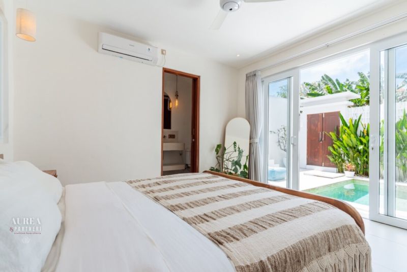 A bright bedroom in a villa with access to a terrace and a view of the pool.
