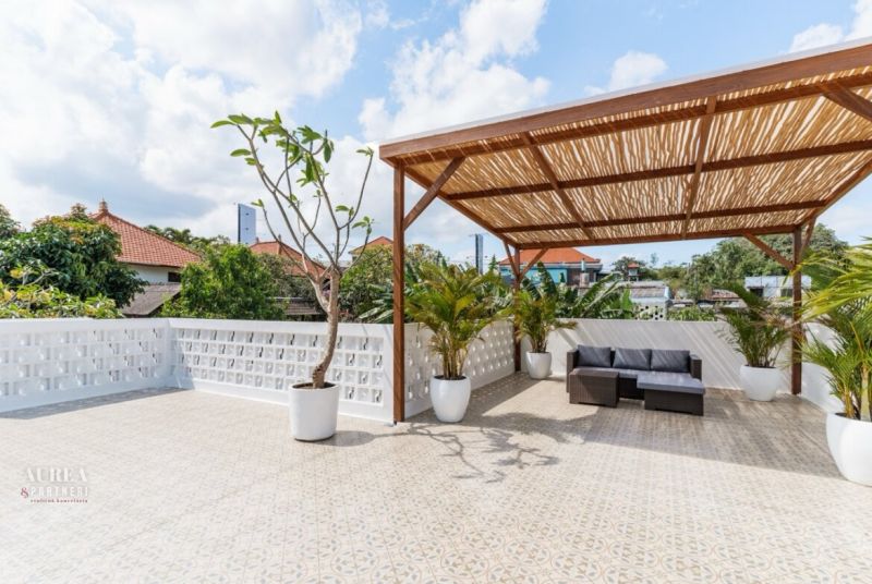 A terrace in a villa in Bali with a pergola, plants, and rattan seating.