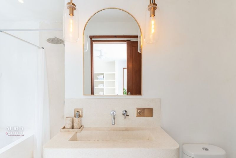 The bathroom of the villa with a round mirror, lights, and a natural stone sink.
