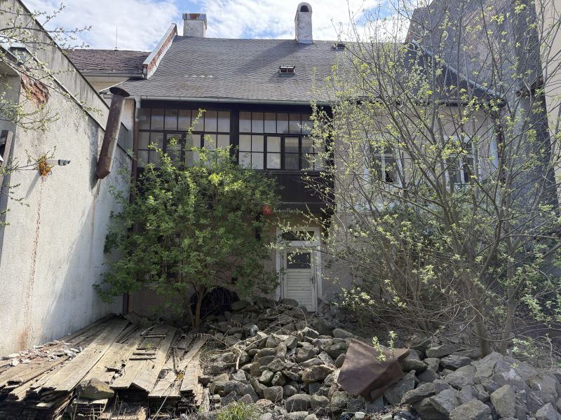 A family house in Kremnica, overgrown yard, old wooden fence, stones on the ground.