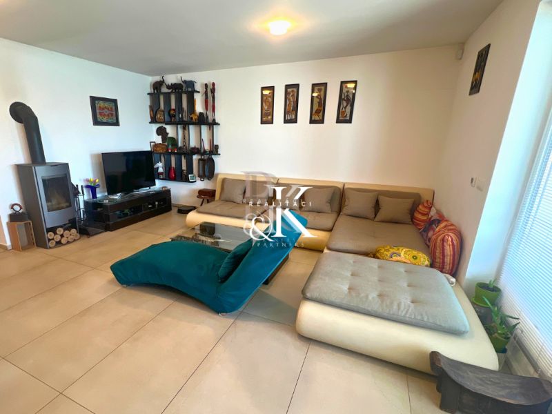 Living room in a family house with a tiled stove, sofa, and shelves on the wall.