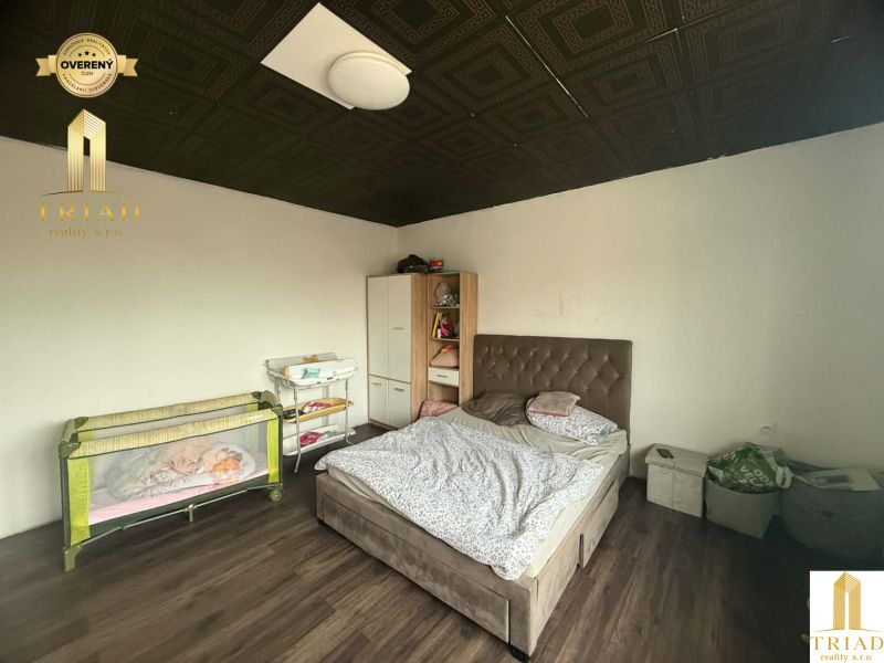 A bedroom in a family house with a wood-decor floor, a bed, and a baby crib.