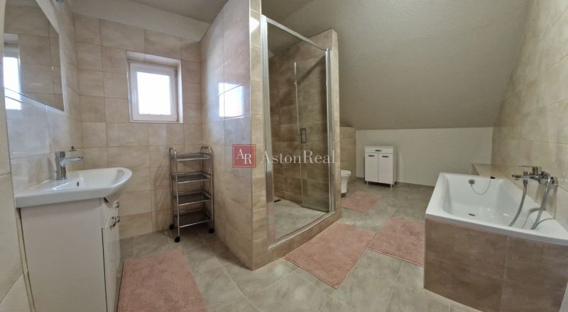 A bathroom in a family house with a bathtub, shower, and tiles in neutral tones.
