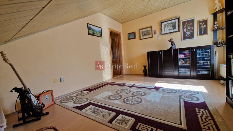 A room in a family house with a carpet, a floor with a wooden decor, and a guitar in the corner.
