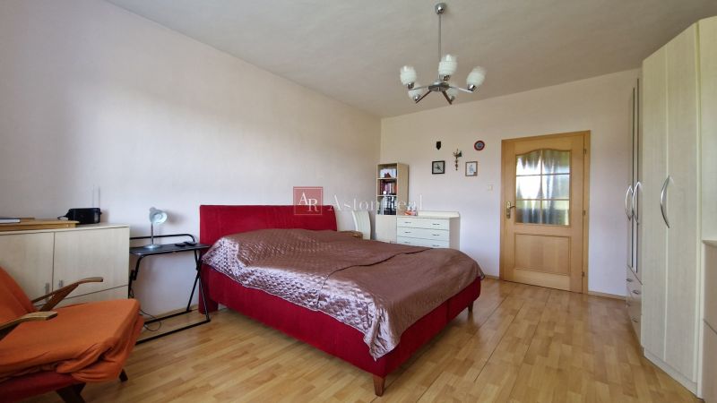 A bedroom in a family house with a red bed and a wooden decor floor.
